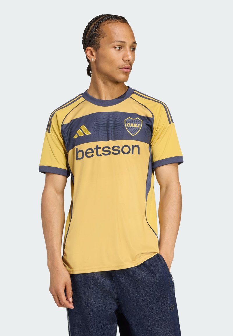 Gelbes und marineblaues Sporttrikot mit kurzen Ärmeln, ausgestattet mit dem "betsson"-Logo, dem "CABJ"-Emblem und gestreiften Akzenten auf den Schultern.
