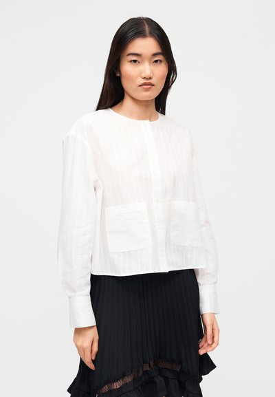 Λευκό, ριγωτό κοντό πουκάμισο με κουμπιά, μακριά μανίκια και δύο μπροστινές τσέπες, συνδυασμένο με μαύρη πλισέ φούστα.