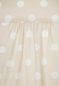 Tessuto beige con grandi pois bianchi e trama arricciata lungo il bordo inferiore. Materiale leggero e leggermente trasparente.