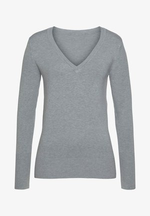 Henkilö harmaassa pitkähihaisessa paidassa ja ruudullisissa naruhousuissa, valkoiset lenkkarit jalassa, nojaa beigeen vintage-avoautoon ulkona.