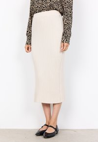 Beige gerippter Midirock mit einem eng anliegenden Bund und ausgestelltem Saum. Kombiniert mit schwarzen Lackballerinas, was einen klaren, strukturierten Look schafft.