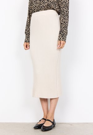 Beige gerippter Midirock mit einem eng anliegenden Bund und ausgestelltem Saum. Kombiniert mit schwarzen Lackballerinas, was einen klaren, strukturierten Look schafft.