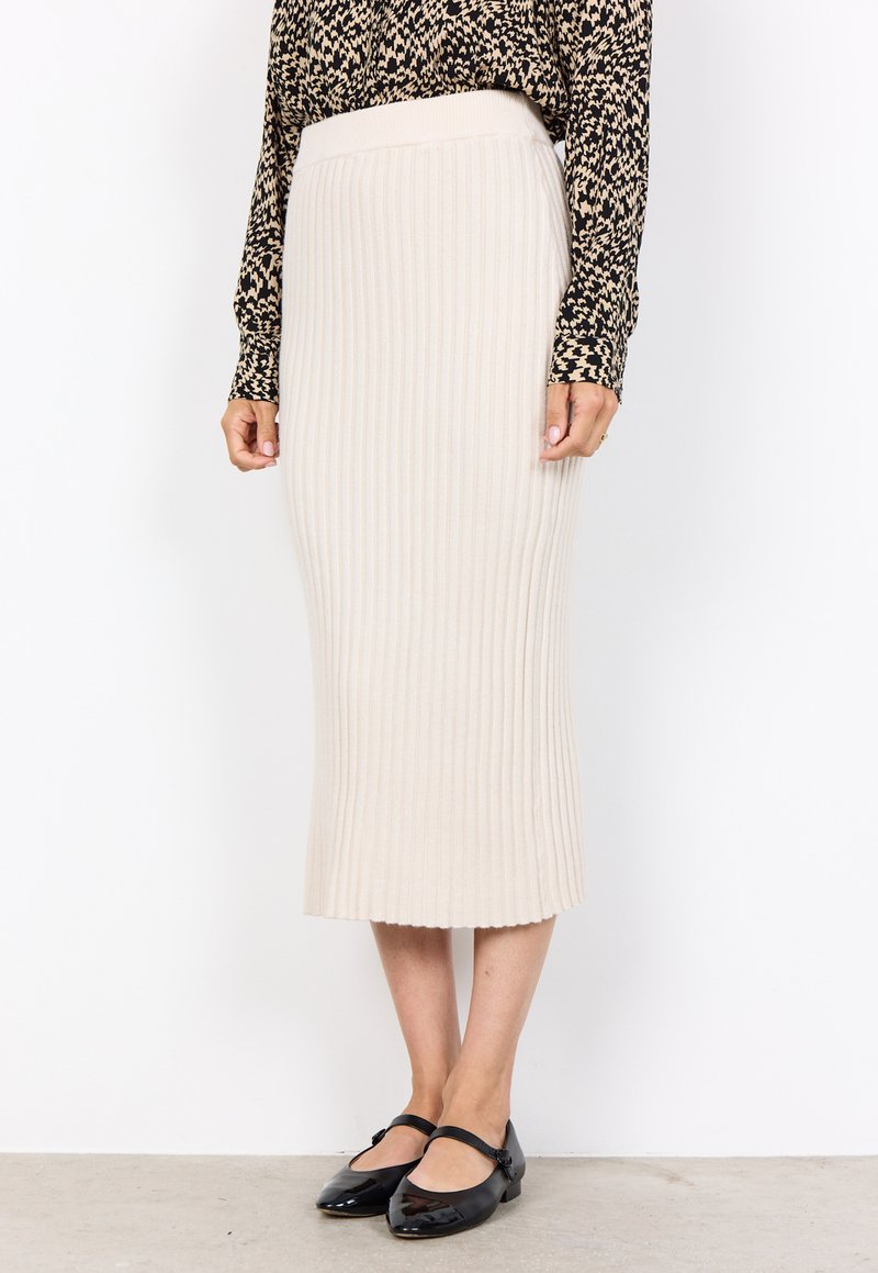 Beige gerippter Midirock mit einem eng anliegenden Bund und ausgestelltem Saum. Kombiniert mit schwarzen Lackballerinas, was einen klaren, strukturierten Look schafft.