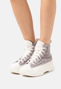 Grå och vita högskor med en texturerad tygöverkappa, kraftig vit sula och vita snören. Mjuk fleecefoder i kragen.