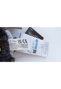 Soft plush toy with dark fur, gray accents, and a label displaying care instructions and compliance symbols, against a white background.