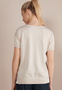 Beige kortærmet sweater med en afslappet pasform, blød tekstur og ribbet kant. Lige rygdesign med sideslids for ekstra komfort.