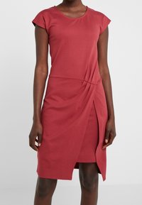 Vestido burdeos hasta la rodilla con mangas tipo capa, escote redondo, diseño torcido en la cintura y abertura lateral para un detalle adicional. Textura de tela suave.