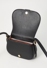 Černá kožená crossbody taška s otevřeným klopním, ukazující světle růžovou vnitřní podšívku a zlaté magnetické uzávěry na bílém pozadí.