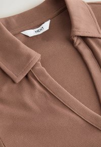 Polo shirt marrone a coste con colletto strutturato e scollatura a V. Etichetta con la scritta "NEXT". Tessuto morbido e testurizzato con cuciture visibili.