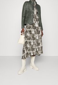 Zelená prošívaná bunda, šedobílé vzorované šaty, bílá kabelka a bílé robustní boty. Hladká textura, současný design.