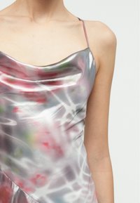 Robe en satin à col bénitier avec fines bretelles, présentant un motif abstrait multicolore aux tons roses, verts et argentés. Texture lisse.