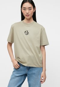 Tricou din bumbac de culoare verde deschis, cu mâneci scurte, guler rotund și un grafic de logo negru pe piept; croi lejer și textură moale.