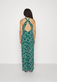 Grønn blomsterdrakt med halterneck og åpen ryggdetaljering. Har en vid benstil og fargerike blomsterdesign overalt.