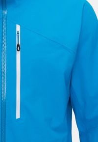 Blaue wasserdichte Jacke aus strukturiertem Stoff, mit einem Reißverschluss über die gesamte Länge und einem dekorativen Ziehband sowie einer kontrastierenden weißen Reißverschlusstasche auf der Brust.