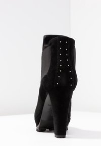 Černé semišové kotníkové boty na vysokém podpatku, se Boční elastickou panelem a stříbrnými nýty podél zadní části, s texturovanou podrážkou pro lepší přilnavost.