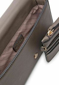 Braune Kunstleder-Handtasche mit goldenen Beschlägen, das Innere hat ein rosa Futter mit leichten Streifen, eine Reißverschlusstasche und ein Logoschild. Kompakte Form.