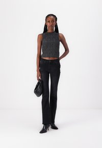 Fekete, textúrált részletekkel díszített cropped top sötét, flare szabású farmernadrággal, amely stud díszítéssel készült, egy fekete táskával és magassarkú csizmával kiegészítve.