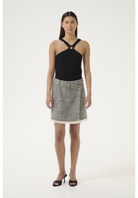 Musta halterneck-top, jossa on pyöreä varuste, yhdistettynä lyhyeen houndstooth-kuosiseksiin, jossa on röyhelöhelma.