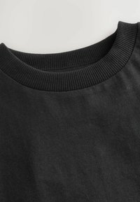 Close-up of a black crewneck sweatshirt showing ribbed collar and smooth fabric texture.