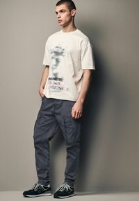 Creme oversized t-shirt med et sløret grafisk tryk, parret med slim-fit grå cargo bukser med sidelommer og sneakers.