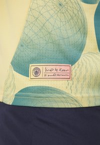 Tričko s krátkým rukávem vyrobené z světle žluté látky s modrými geometrickými vzory, štítek s nápisem "Imp 4 Ever", námořnický lem a texturovaný povrch.