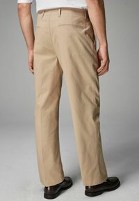 Pantaloni bej cu un design drept, având buzunare la spate și o țesătură fină, ușoară. Asortați cu pantofi loafer negri.
