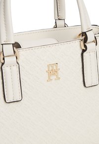 Λευκή δερμάτινη τσάντα χειρός με ανάγλυφο σχέδιο, χρυσό λογότυπο "TH" και διπλές λαβές συνδεδεμένες με χρυσούς κρίκους.