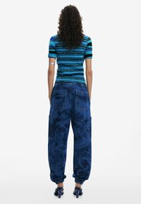 Striped blue knit top with short sleeves; blue denim cargo pants with side pockets; model wearing dark blue heeled sandals; back view.