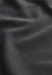 Gros plan d'un tissu texturé gris foncé avec de petits points en relief, espacés uniformément, créant un motif en forme de maille et des plis délicats.