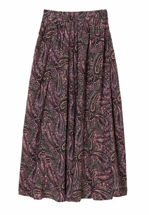 Kvinde iført et langt, højtaljet skørt med lilla paisley-mønster og beige slip-on sko, stående mod en ensfarvet baggrund.