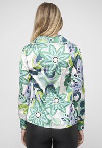 Vícebarevná halenka s květinovým vzorem v odstínech zelené a fialové, vyrobená z lesklého materiálu, s límečkem a manžetami na knoflíky.