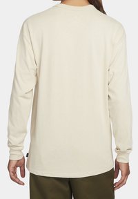 Long-sleeve, cream-colored shirt made from soft cotton. Features a rounded neckline and straight hem. Simple design, no visible patterns.