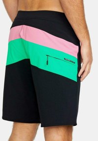 Bañador negro con bloques de color en diagonal en rosa y verde, con un bolsillo con cremallera en el lateral y detalle de etiqueta de marca.