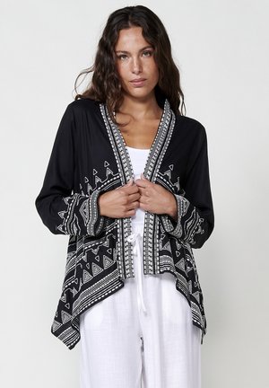 Black long-sleeve kimono-style jacket with white geometric patterns, open front, and accent trim. Lightweight fabric with relaxed fit.