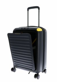 Valise rigide noire avec texture rainurée, accent jaune, poignée rétractable et roues roulantes lisses. Partiellement ouverte avec l'intérieur visible.
