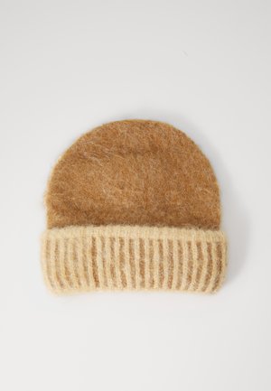 Brown knit beanie with a ribbed cream cuff. Features a soft, fuzzy texture and rounded top. Made from warm, wool-like material.