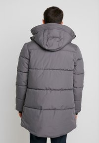 Cappotto imbottito grigio con design trapuntato, cappuccio regolabile e vestibilità di lunghezza intermedia. Texture liscia con un profilo posteriore completo.