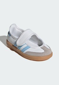 Biele topánky s suchým zipsom, šedou semišovou špičkou a svetlomodrými akcentmi. Gumová podošva s textúrovaným gripom. Zaoblený dizajn.