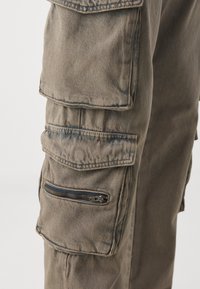 Pantaloni cargo in un colore oliva tenue, dotati di più tasche e una tasca laterale con zip. Realizzati in un tessuto durevole e strutturato.