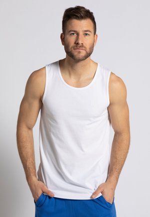 Weißes Baumwoll-Tanktop mit Rundhalsausschnitt und ärmellosem Design, mit einem dezenten Logo auf der Vorderseite. Getragen mit blauen Shorts.