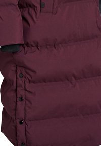Close-up of maroon puffer jacket with black snap buttons along the side and a ribbed black cuff visible on the sleeve.