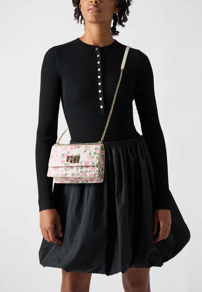 Μικρή ροζ τσάντα ώμου με λουλουδάτο σχέδιο, χρυσές λεπτομέρειες και αλυσίδα. Φορεμένη πάνω από ένα μαύρο ριμπ κορμάκι και μια φουσκωτή μαύρη φούστα.