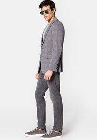 Szary, w kratkę marynarka, szary t-shirt, dopasowane szare spodnie i szare sneakersy. Dodatki to zielone okulary przeciwsłoneczne. Dopasowany krój, gładka tekstura.