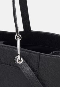 Černá kožená taška přes rameno s texturovaným povrchem, vybavená stříbrným kovovým kruhovým spojem a plochými ramenními popruhy. Vnitřek je viditelný.