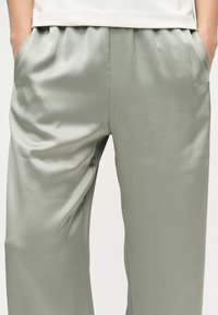 Άτομο που φοράει ανοιχτό γκρι υφασμάτινο παντελόνι με τα χέρια στις πλαϊνές τσέπες και λευκό τοπ, εμφανίζεται από τη μέση έως το μέσο του μηρού.