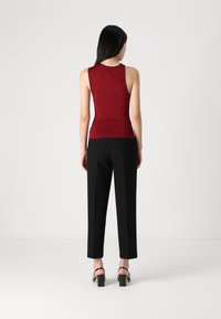 Top sin mangas color vino con detalle fruncido en la parte de atrás, combinado con pantalones negros de corte ajustado y sandalias de tacón cuadrado.