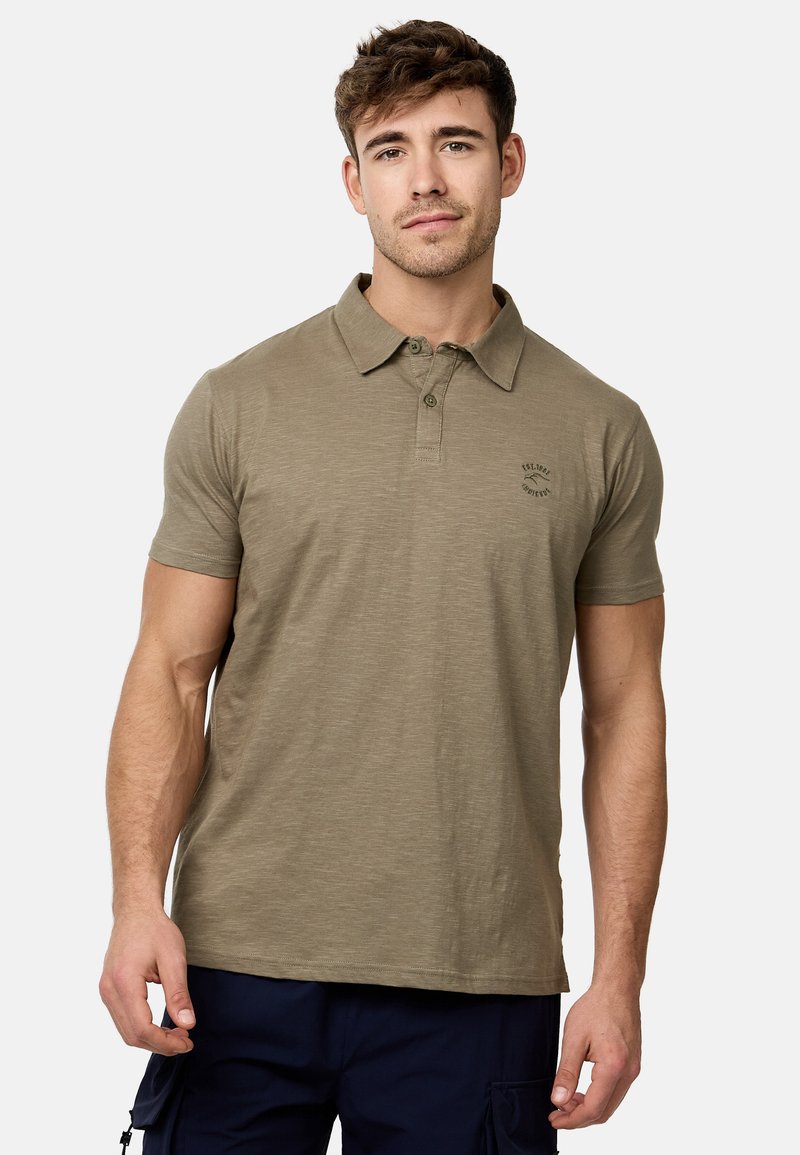 Polo olive en tissu doux, avec un col à trois boutons, des manches courtes et un petit logo sur la poitrine gauche.