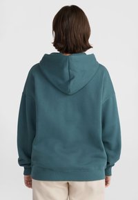 Felpa oversized color verde acqua con cappuccio sul retro, vestibilità rilassata e polsini a coste. Texture morbida e design senza cuciture, senza accenti hardware visibili.
