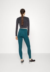 Czarny, długi rękaw, krótki top z teksturowanym wykończeniem, zestawiony z turkusowymi legginsami w wysokim stanie z gładkiego materiału oraz czarnymi butami sportowymi.