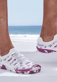 Weiße Sportschuhe mit lila Akzenten und strukturierten Mustern, die eine leichte Strickoberfläche, Schnürdetails und eine strapazierfähige Gummisohle aufweisen.